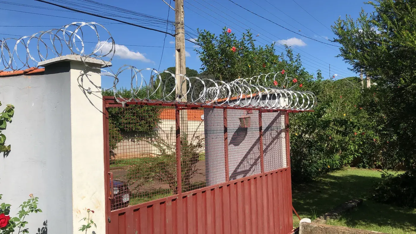 Concertina instalada acima de um portão vermelho e de pilares brancos